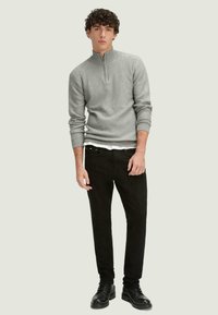 Suéter gris de cuello con cremallera en punto texturizado, combinado con jeans ajustados negros y botas negras con cordones. Diseño simple y moderno en colores neutros.