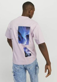 Ljusrosa bomullströja med en stor abstrakt blå grafisk design och geografiska koordinater på baksidan, med en avslappnad passform och korta ärmar.