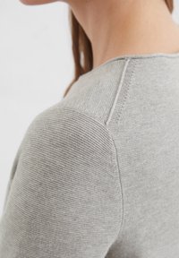 Grijze gebreide trui met een gemêleerde afwerking, voorzien van een ronde halslijn en een gladde schoudernnaad. Zachte stof valt elegant.