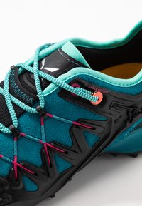 Turkise sportssko med sorte accenter, tekstureret overdel og pink snørre. Inkluderer en markant "CLIMB" detalje og mønstret sål for bedre greb.
