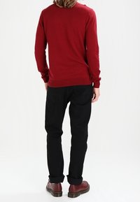 Rode trui gemaakt van een zacht materiaal, gecombineerd met zwarte broek. Zwarte schoenen hebben een ronde neus en een contrasterende zool.