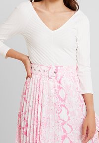 White ribbed top with a V-neckline and three-quarter sleeves, paired with a pleated pink and white patterned skirt featuring a belt.