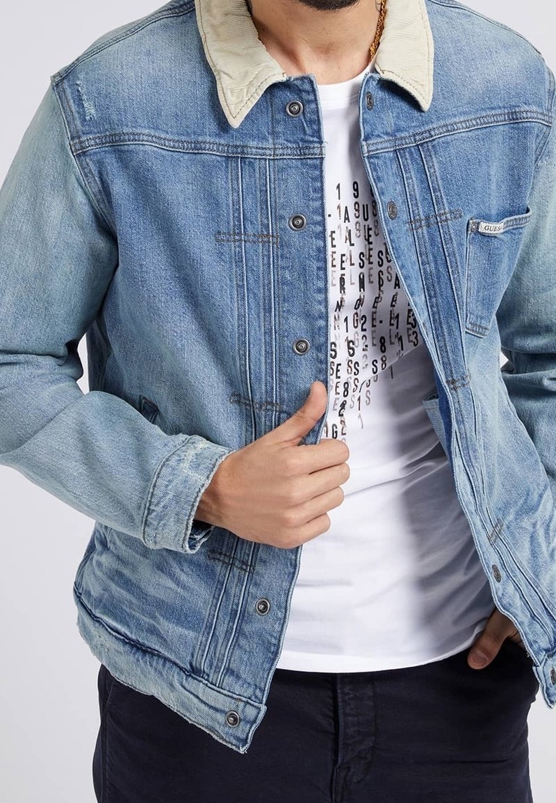Light blue denim jacket with a cream-colored collar, featuring a button closure, two chest pockets, and distressed detailing. White printed t-shirt underneath.