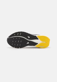 Suola di scarpa da corsa nera e gialla con gomma texturizzata, caratterizzata da un logo PUMAGRIP ben visibile e un battistrada a motivo per una migliore aderenza.