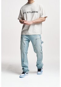 Beige t-shirt with "2Y STUDIOS" print, light blue denim cargo pants with pockets, and black Nike sneakers with blue accents.