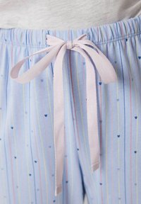 Lichtblauwe pyjamashorts met verticale strepen in roze en geel, versierd met kleine hartpatronen en een roze satijnen strik in de taille.