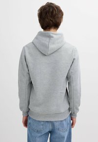 Sudadera gris con capucha, hecha de tejido suave, que presenta un bolsillo tipo canguro y puños acanalados. Combinada con jeans de color azul claro.