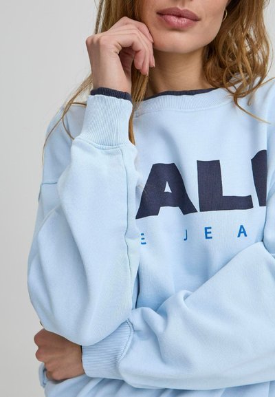 Lyseblå sweatshirt med ribbet hals og mansjetter, stor mørkeblå tekst på forsiden, og en avslappet passform.