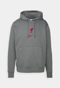 Sweat à capuche gris avec poche avant, arborant un logo brodé rouge de Liverpool FC et le swoosh Nike, fabriqué en tissu doux et texturé.