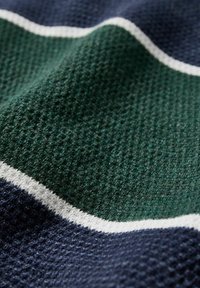 Vävt textil med en blandning av mörkgrön, marinblå och vita ränder, med en texturerad yta och subtila mönster genom hela.