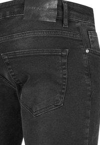 Mustmustest denim püksid on tekstuuriga viimistlusega, vöökoht on kaunistatud nahast bränditagiga ja seljal on üks õmmeldud tasku.