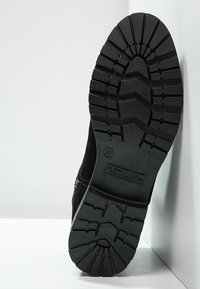 Suela de zapato de goma negra con un patrón de banda de rodadura prominente, con la marca Tamaris. La parte superior está hecha de un material suave y texturizado.