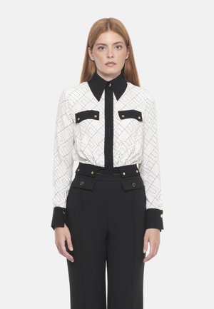 Blusa bianca e nera a fantasia con colletto a punta e bottoni dorati, abbinata a pantaloni neri a vita alta con dettagli a bottoni.