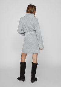 Robe grise en tricot avec un col bénitier et une taille ceinturée. Dotée de manches longues et d'un ourlet arrivant au-dessus du genou. Portée avec des bottes noires jusqu'aux genoux.