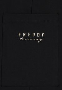Tessuto nero con una tasca texturizzata caratterizzata dal testo impresso "FREDDY" in lettere maiuscole metalliche e "training" in uno stile corsivo.
