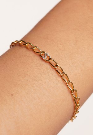 Gold chain bracelet featuring oval links with a small, embellished accent in the center. Smooth texture against skin.