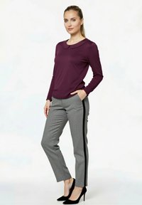 Bordeauxrotes Langarmoberteil mit Peter-Pan-Kragen, kombiniert mit grauen karrierten Hosen mit schwarzem Seitenstreifen und schwarzen, spitz zulaufenden Absätzen.