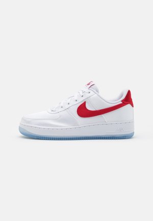 Baskets basses blanches avec le logo Nike rouge, languette de talon rouge, lacets blancs et semelle en caoutchouc translucide bleue sur fond uni.