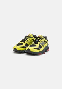 Neon yellow and black athletic shoes with mesh and synthetic upper, featuring a thick sole with red accents and prominent logo detail.
