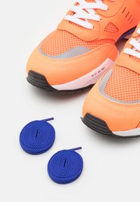 Ljusa orangea träningsskor med mesh- och mockakvaliteter, med vita snören och blå flätade snören bredvid dem.