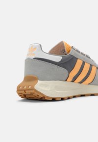 Sneaker in suede e mesh grigio con strisce arancioni, dettagli bianchi e suola in gomma. Tallone testurizzato e etichetta del marchio visibili.