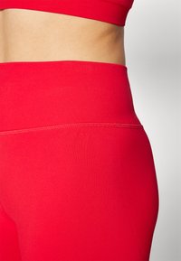 Røde treningstights med høy midje, elastisk materiale, sømløst design og glatt tekstur. Ingen synlige mønstre eller beslag.