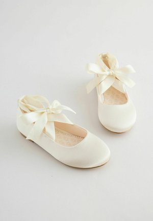 Białe baleriny z fakturowanego materiału, z zaokrąglonym noskiem, niskim obcasem oraz kokardkami z satyny na paskach wokół kostki.