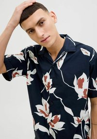 Camisa de botones de manga corta en color marino con un patrón floral en blanco y marrón. Presenta un cuello relajado y botones negros. Textura de tela suave.