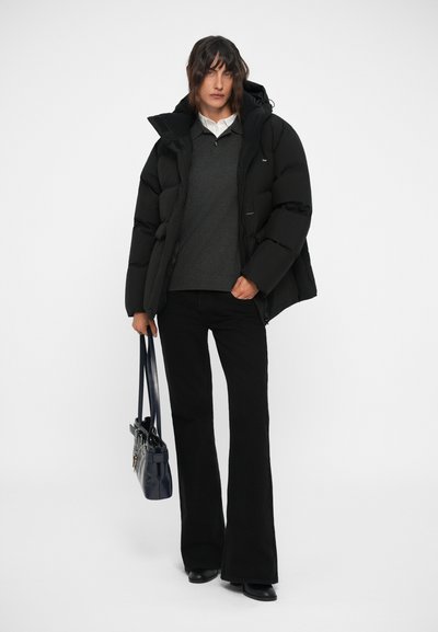 Doudoune noire avec capuche, superposée sur un pull gris. Un pantalon noir évasé et un sac à main bleu marine complètent la tenue.