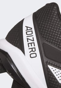 Musta-valkoinen urheilukengä, jossa on teksturoitu päällinen, korostettu "ADIZERO" brändäys ja muotoiltu pohja parannettuun pitoon.