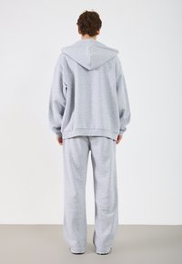 Hallide sussul, millel on kapuuts ja laiad varrukad, koos vastavate hallide dressipükstega. Valmistatud pehmest kangast, millel on mugav lõige.