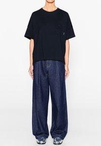 Camiseta negra de manga corta con bolsillo y un diseño texturizado; combinada con unos vaqueros de pernera ancha en denim azul oscuro y unos zapatos plateados brillantes.