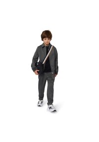 Grå zip-up jacka och matchande byxor, svart t-shirt under, med vita och svarta sneakers. Axelväska med ett mönstrat rem.