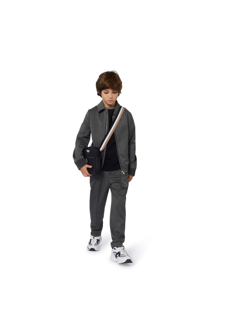 Grå hettejakke med glidelås og matchende grå bukser, kombinert med en svart T-skjorte og hvite joggesko. En liten svart crossbody-veske med en stripete stropp.