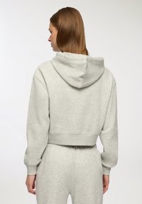Szara, krótkopedna bluza z kapturem o miękkiej fakturze, z mankietami na rękawach. Projekt obejmuje luźny krój i elastyczny pas.