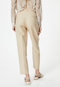 Beige op maat gemaakte broek met een rechte pasvorm, voorzien van een achterzak, gecombineerd met lichtgekleurde sandaal met bandjes. Glad stofoppervlak.