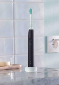 Spazzolino elettrico Philips Sonicare con manico nero, base bianca e testa con setole blu e bianche, posato su un piano in marmo.