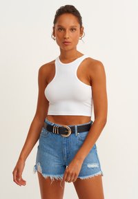 Vit ribbad cropped topp kombinerad med slitna blå denimshorts och ett svart bälte med ett guld cirkulärt spänne.