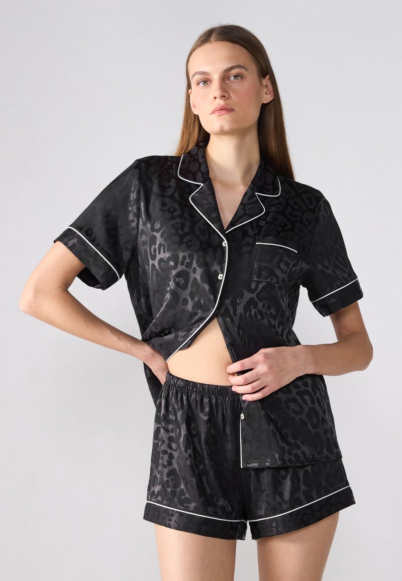 Ensemble de pyjama à manches courtes avec imprimé léopard noir et finitions blanches ; comprend un haut à col avec une poche et un short avec taille élastique.