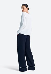 Biely textúrovaný sveter s výstrihom do oblúka, nosený s tmavomodrými širokými nohavicami s bielym lemom na spodnom okraji.