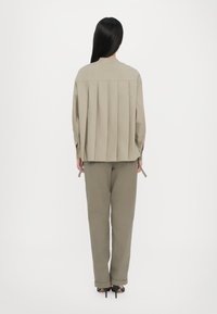 Beige pleated top with a high neckline and long sleeves, paired with matching tapered pants. Lightweight fabric and subtle texture.