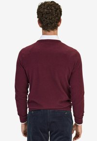 Burgundy neulepaita pitkillä hihoilla ja pyöreällä pääntiellä, yhdistetty tummansinisiin samettihousuihin, nähtynä takaa.