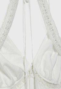 Vêtement blanc avec des détails en dentelle le long de l'encolure et des bretelles, en tissu doux et drapé offrant une apparence légère.