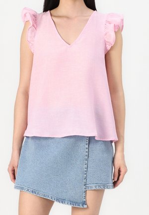 Kvinde iført en lyserød ærmeløs top med flæser på skuldrene og V-udskæring, kombineret med en asymmetrisk lyseblå denimnederdel.