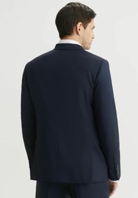 Granatowa marynarka o dopasowanym kroju, z jednolitym rozcięciem z tyłu i czterema guzikami na mankietach. Gładka faktura materiału.