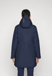 Mörkblå vadderad jacka med huva, med en slät yta och långa ärmar. På baksidan finns en logo nära nacken.