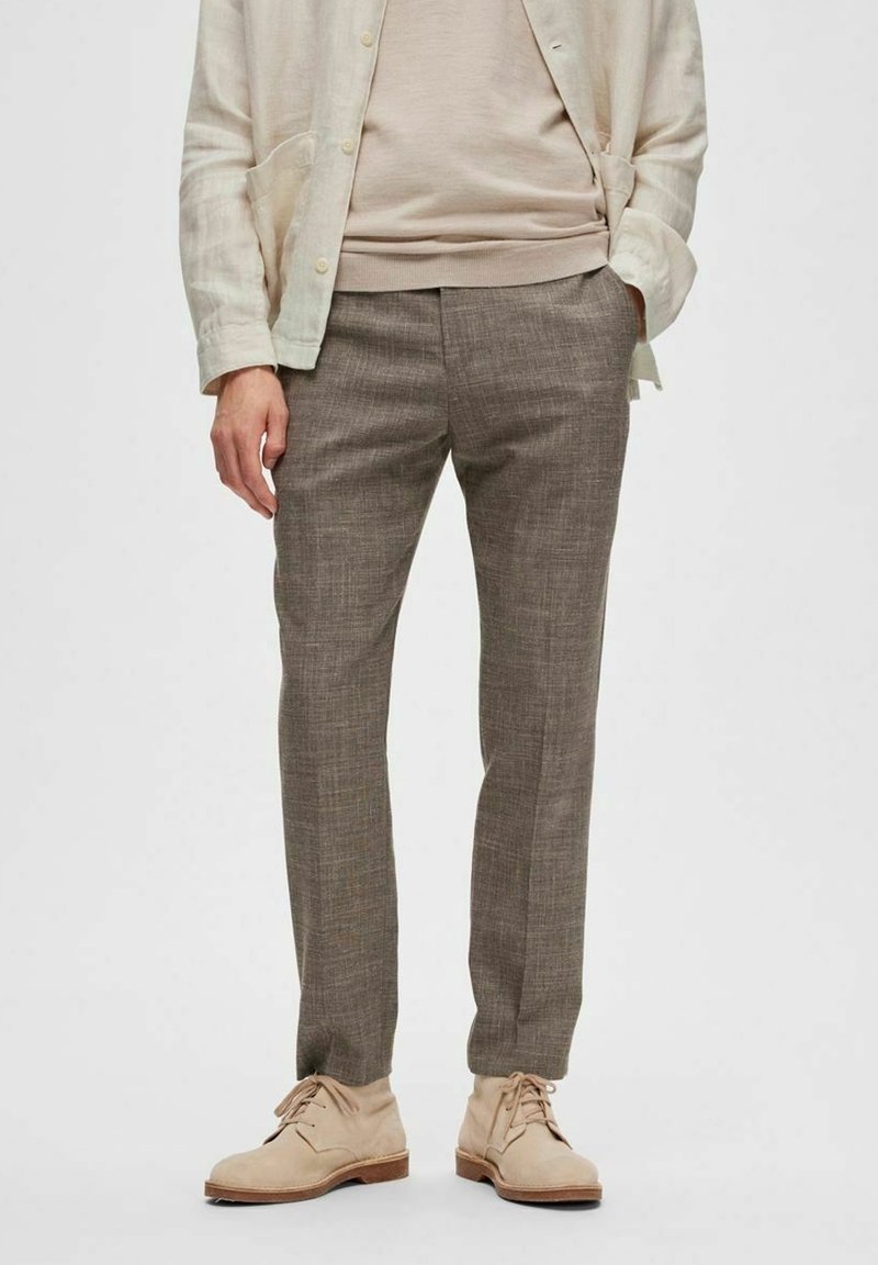 Chemise boutonnée en lin beige clair sur un pull neutre, associée à un pantalon marron texturé et des chaussures claires. Éléments de design simples et modernes.