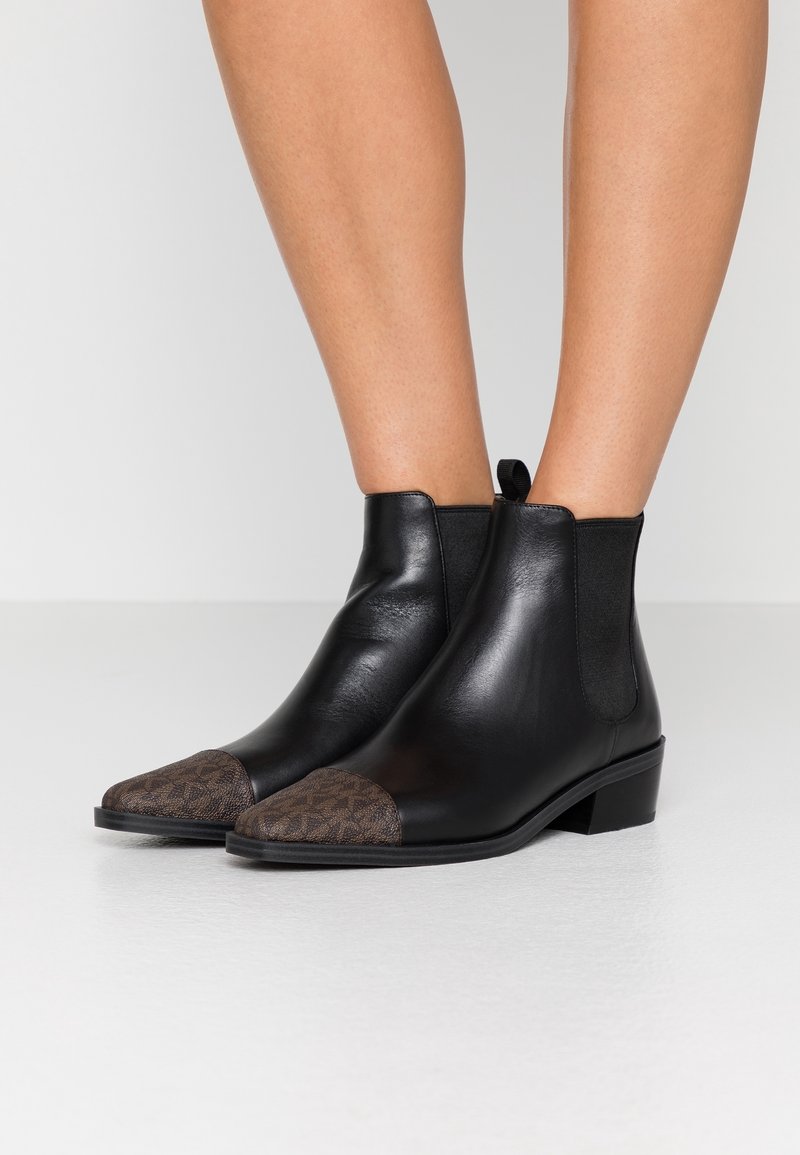 Stivaletti neri in pelle con punta a cappuccio marrone texture. Presentano pannelli elastici laterali e un tacco basso per stabilità e comfort.