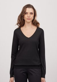 Schwarzer V-Ausschnitt-Pullover mit langen Ärmeln, weicher Textur, figurbetontem Schnitt und geripptem Saum. Einfaches, klassisches Design, das sich gut zum Schichten eignet.