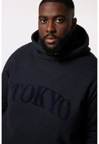 Felpa con cappuccio blu navy realizzata in tessuto morbido, dotata di una grande stampa ad arco "TOKYO" di un blu navy più scuro sul petto.